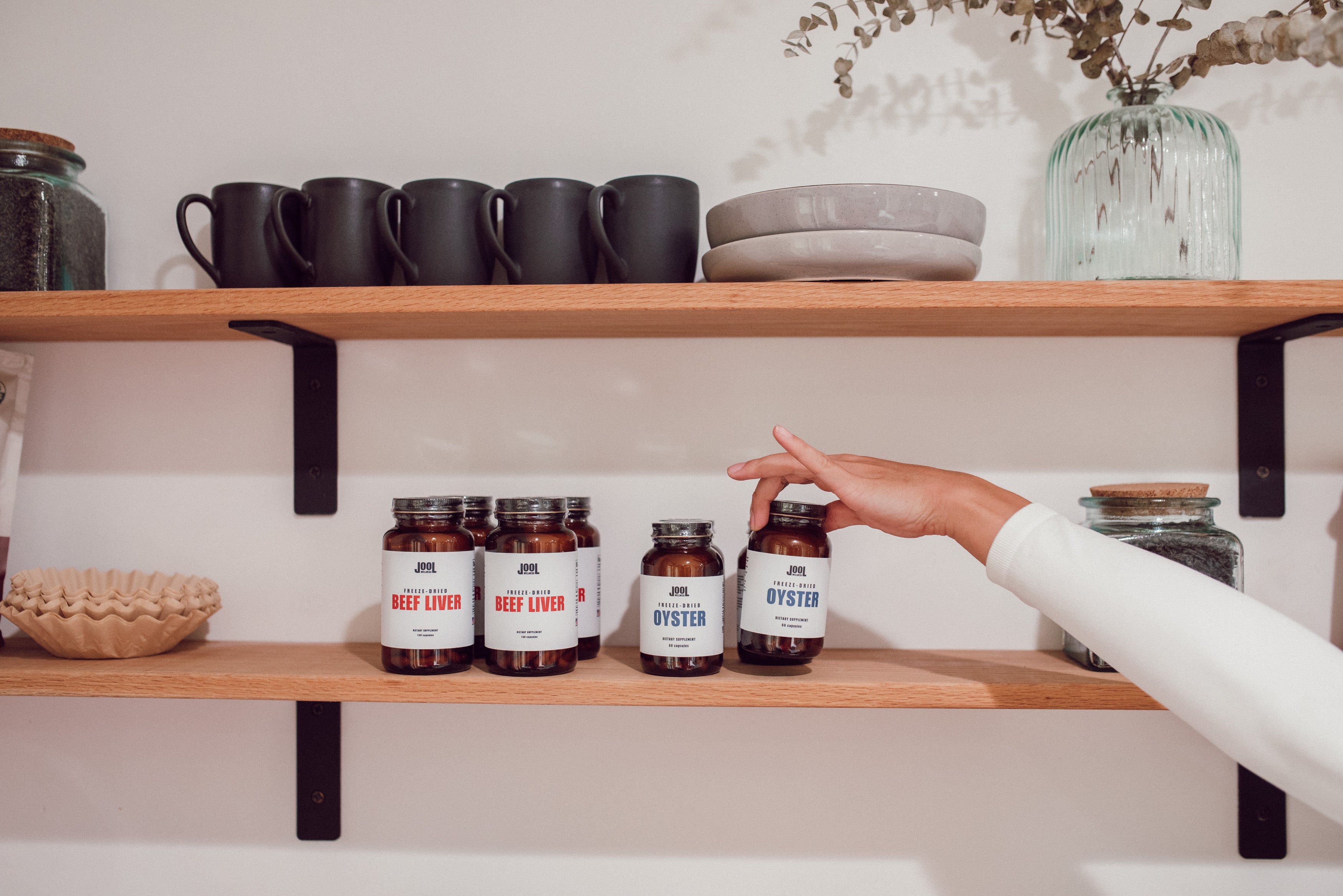 Hand reaching for a supplement bottle on a shelf with other items.